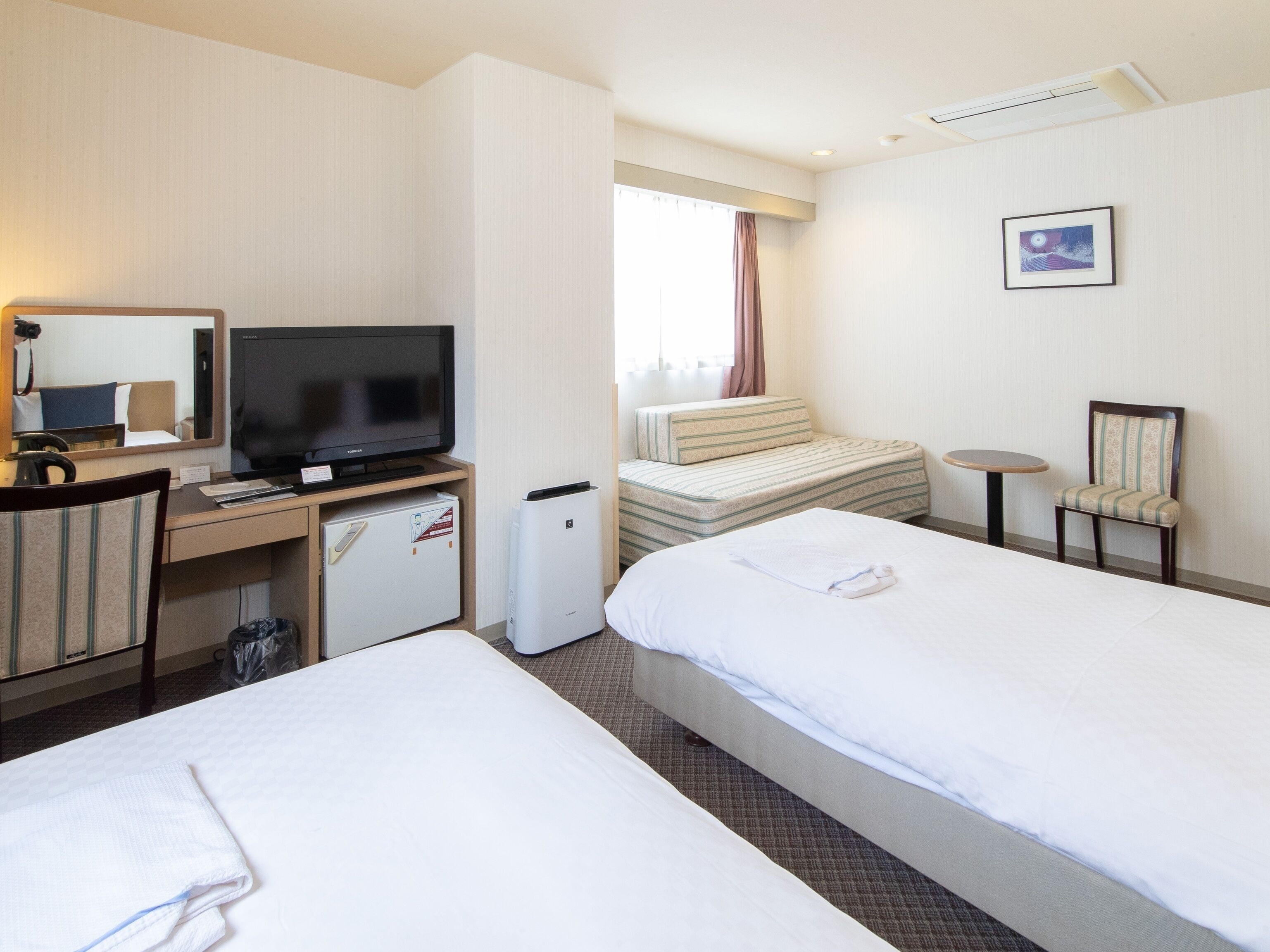 Habitación de hotel con dos camas, un escritorio con televisor, un refrigerador pequeño y una silla.