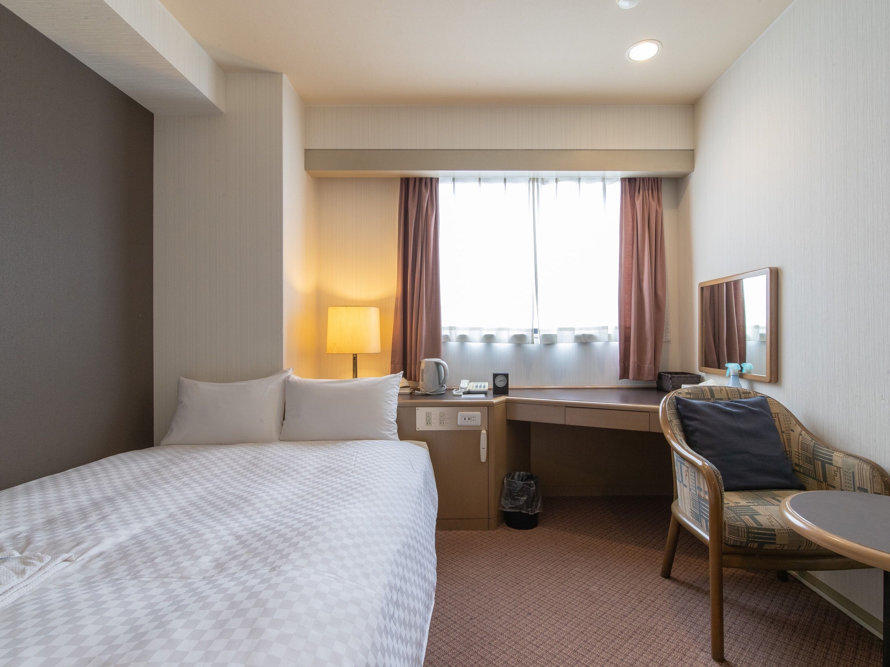 Une chambre d’hôtel avec un lit, un bureau, une chaise et une fenêtre avec des rideaux.