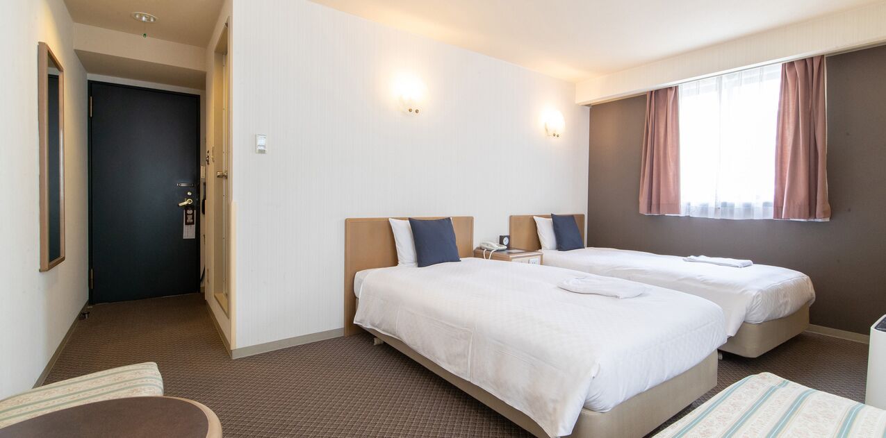 Ein Hotelzimmer mit zwei Betten, einem Schreibtisch, einem Stuhl und einem Fenster mit Vorhängen.