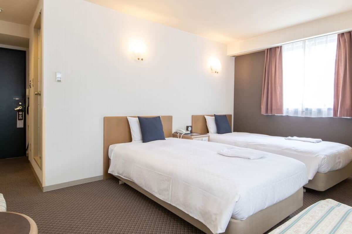 A hotel room with two beds, a desk, a chair, and a window with curtains.