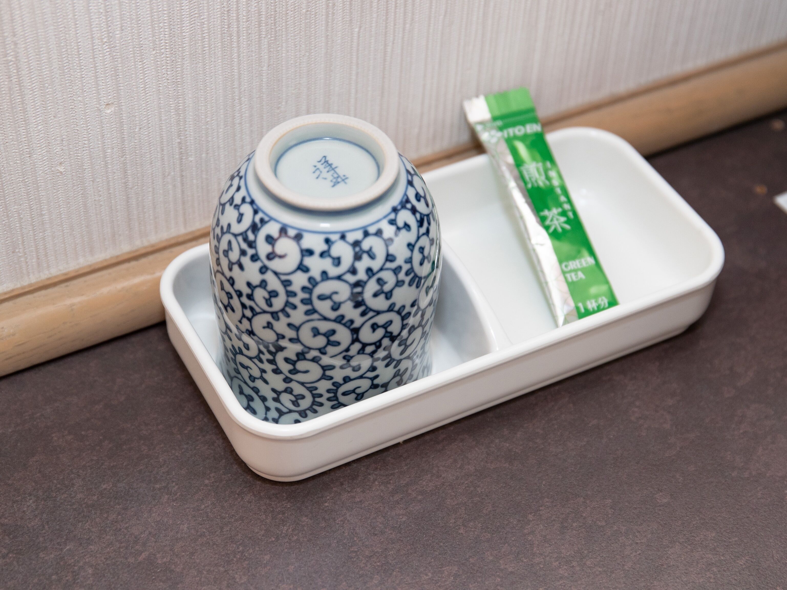 A white ceramic tray with a blue and white patterned vase and a green tea packet.