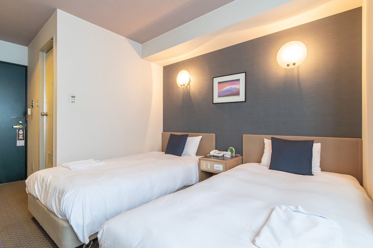 A hotel room with two beds, a nightstand with a phone and a clock, and a picture on the wall.