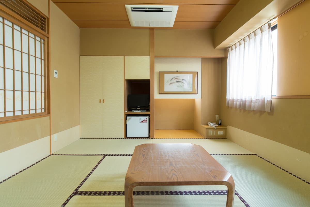 A traditional Japanese room with tatami flooring, a low wooden table, a small cabinet, and a sliding door.