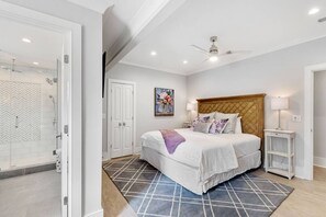 A bedroom with a bed, a nightstand, a lamp, a ceiling fan, and a shower area.