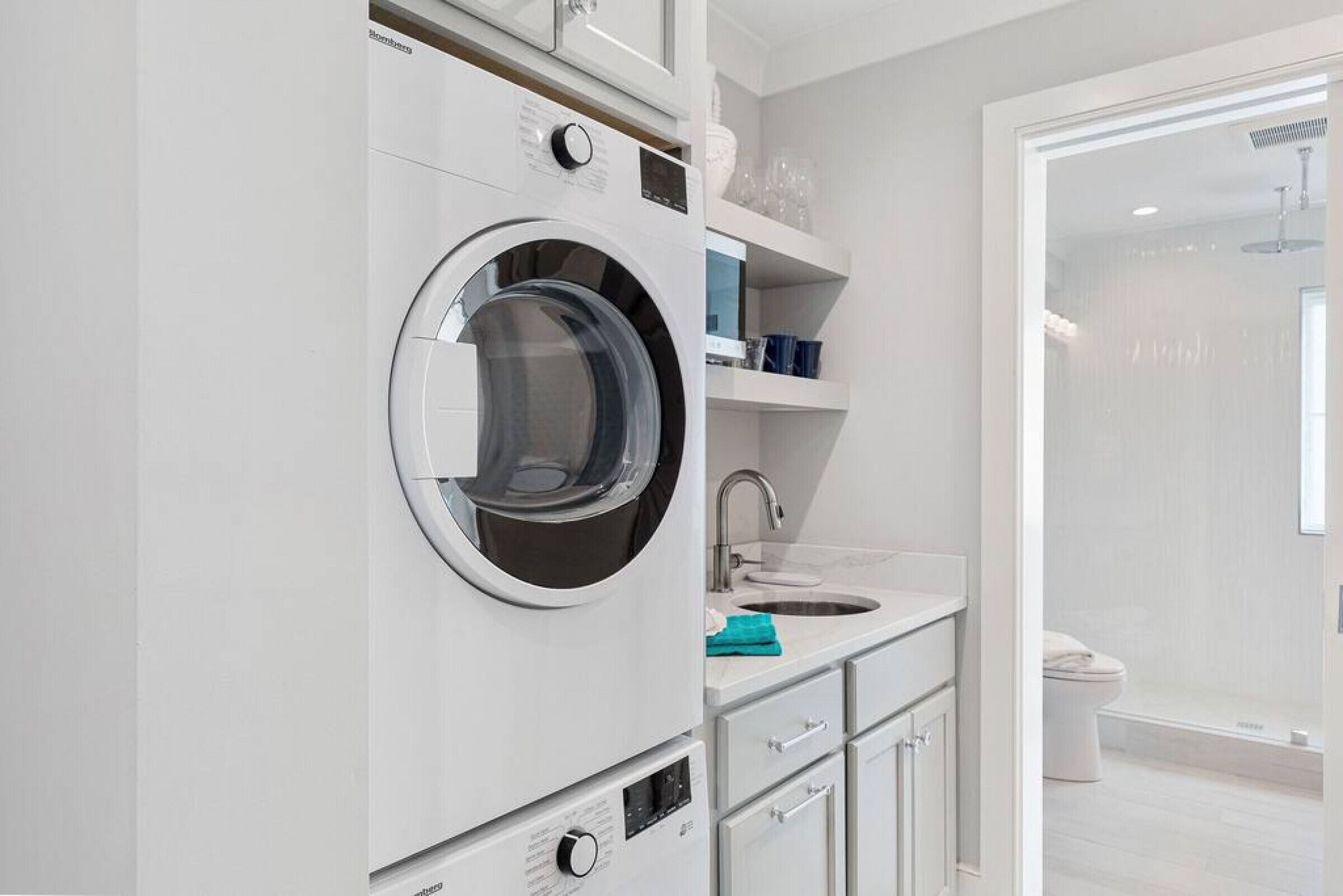 Une salle de bain moderne équipée d’un lave-linge intégré, d’un lavabo et d’un espace douche.
