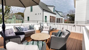A covered outdoor deck with wicker furniture, a round table, and a view of white buildings in the background.