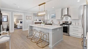 A modern kitchen with white cabinetry, a central island with bar stools, a built-in stove, and a stainless steel refrigerator.