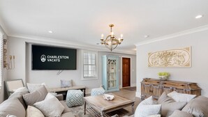 A spacious living room with a large flat-screen TV, a chandelier, and a vintage cabinet.