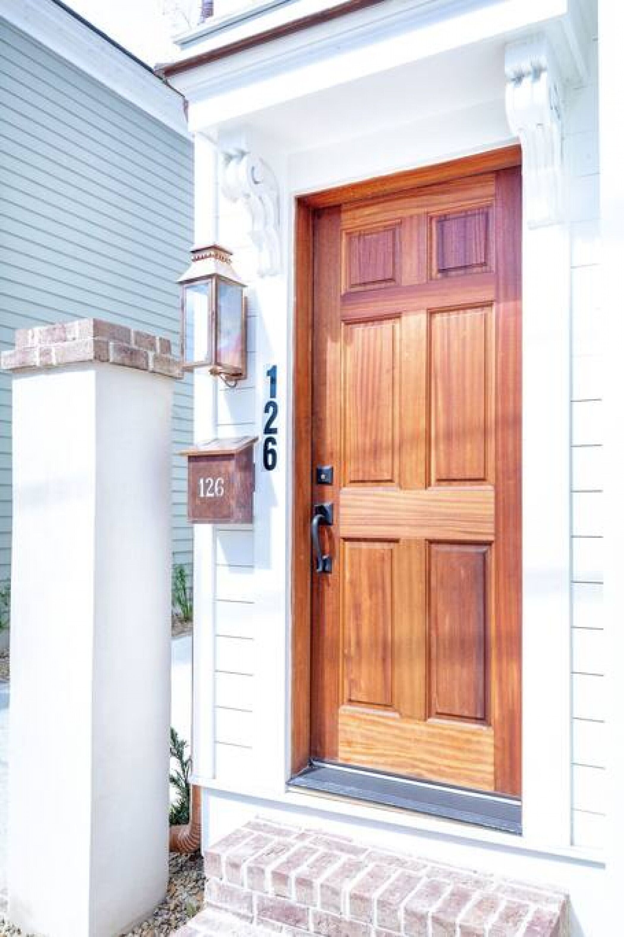 A wooden front door with a number plaque, a mailbox, and a small brick step leading to the entrance.