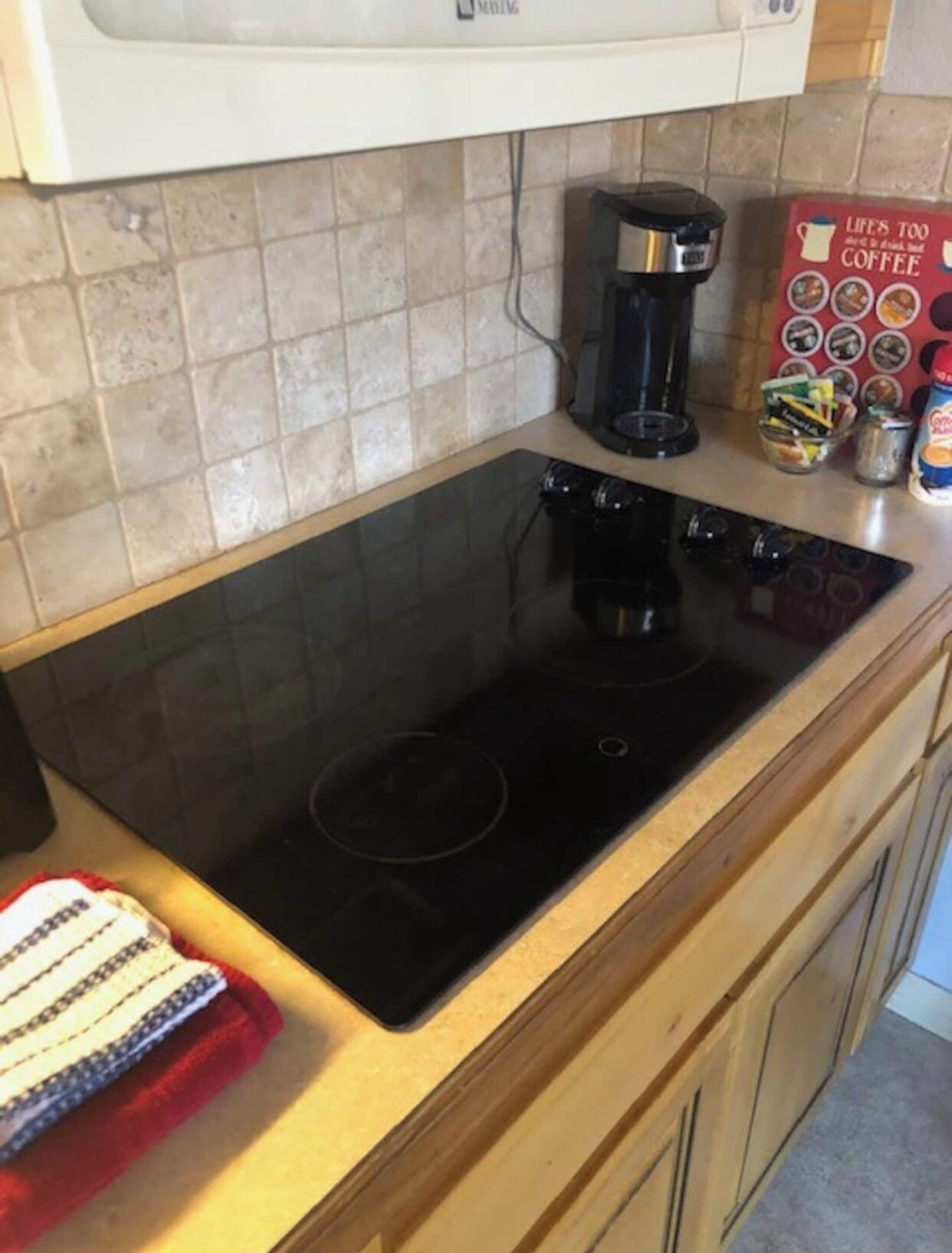Una cocina con placa de inducción negra, una cafetera y un libro de café sobre la encimera.