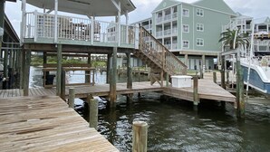 Een pand aan het water met een houten steiger, een overdekt terras met balustrades en een meerlaags gebouw met balkons.