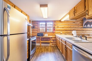 A log cabin kitchen with a refrigerator, stove, microwave, sink, and wooden cabinets.