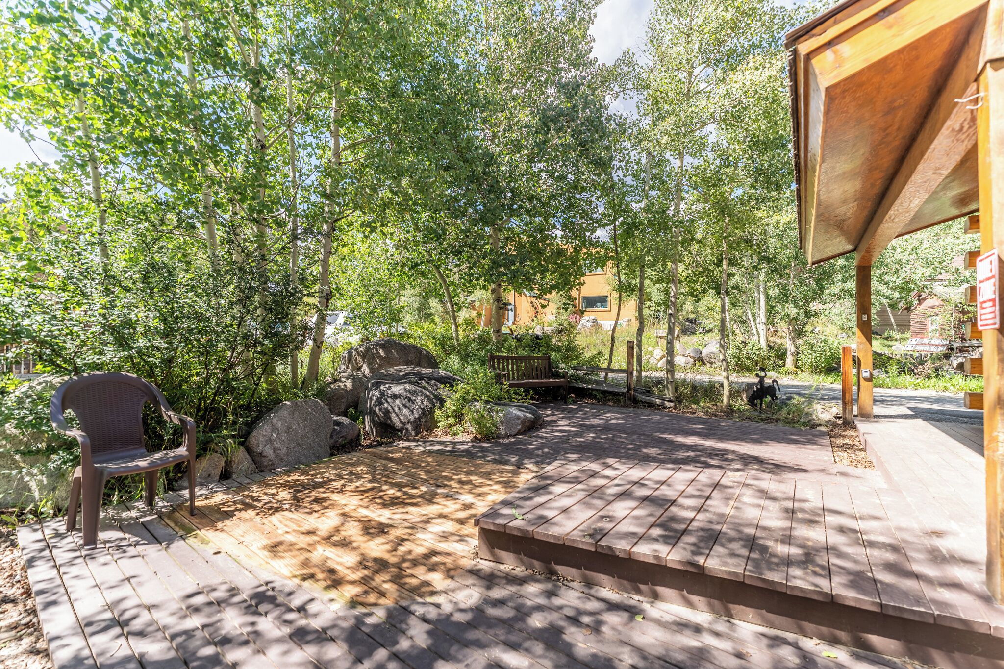 A wooden deck with a bench and a covered area, surrounded by trees and rocks.