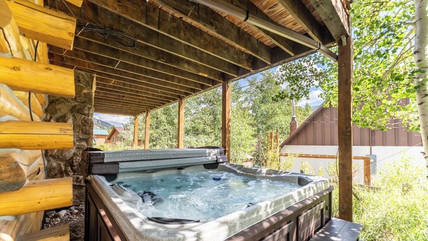 A hot tub under a wooden pergola with stone walls, surrounded by greenery. - 57 Rasor Court by Summit County Mountain Retreats (Keystone)