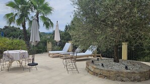 Une terrasse extérieure avec une table ronde en pierre, deux fauteuils et un petit foyer.