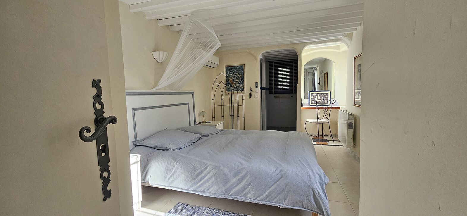 Een slaapkamer met een bed, nachtkastje, stoel en een deur.