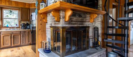 Una chimenea de piedra con repisa de madera, una cocina con armarios de madera y una escalera en espiral.