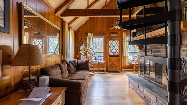 Un interior cálido de cabaña con piso de madera, un sofá, una mesa con una lámpara y una chimenea.