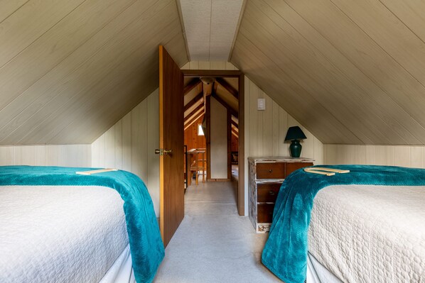A bedroom with two beds, a wooden dresser, and a hallway leading to another room.