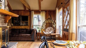 Un interior acogedor de cabaña con paredes de madera, un sillón colgante, un sofá y una mesa de comedor.