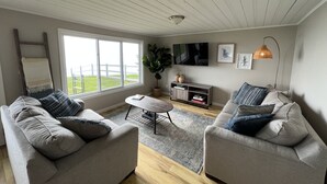 Ein Wohnzimmer mit zwei grauen Sofas, einem Couchtisch, einem Fernseher und einem großen Fenster.