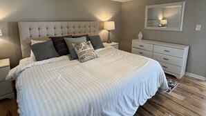 Ein Schlafzimmer mit einem großen Bett, einem Nachttisch, einer Kommode, einem Spiegel und einer Deckenleuchte.