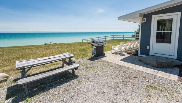 Eine Terrasse am Strand mit Picknicktisch, Grill und Liegestühlen.