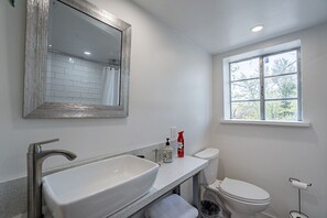 Bathroom features a large vessel sink, rectangular mirror, and a toilet with a view of the outdoors.