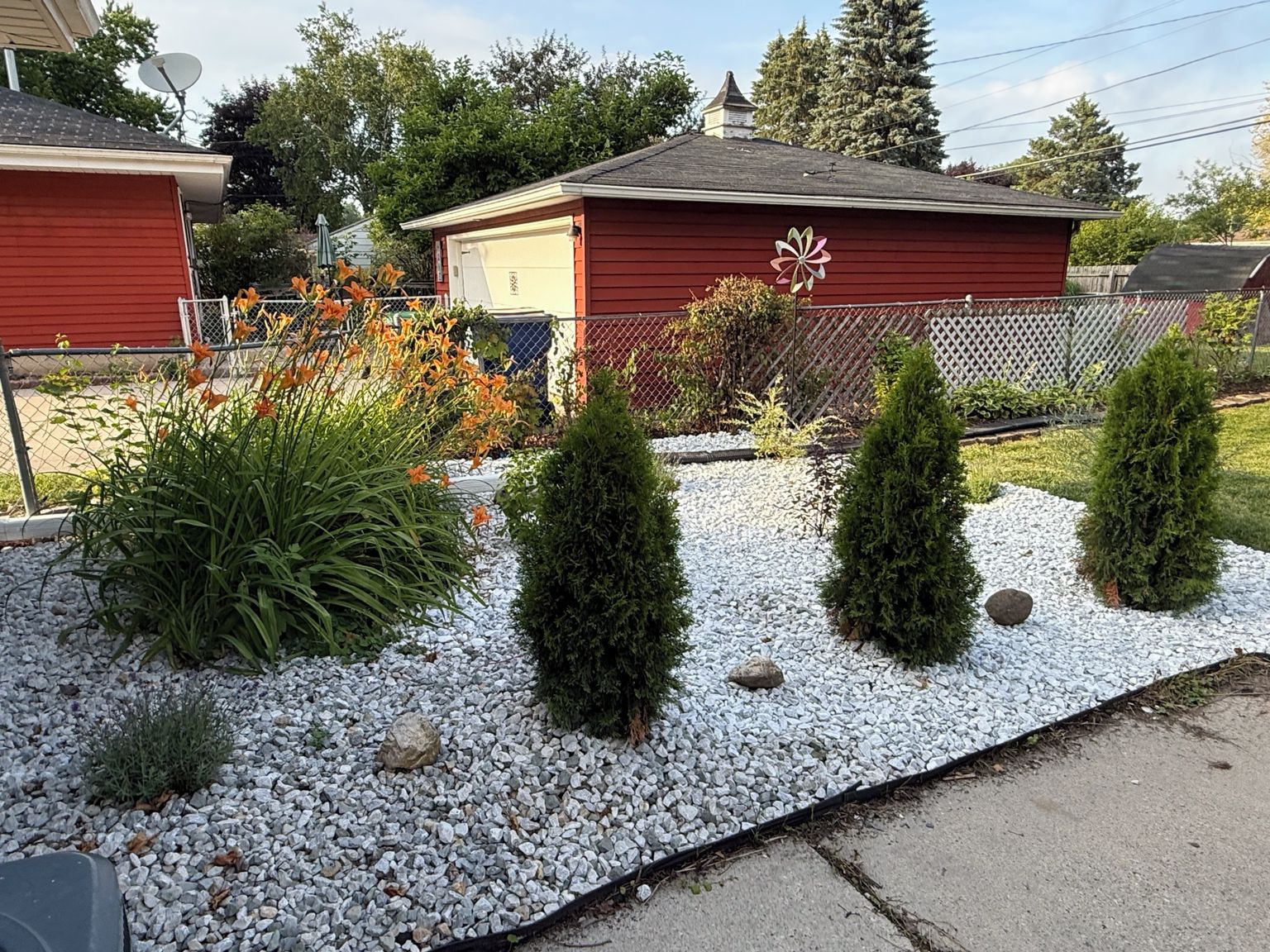 A residential area with a red building, a gravel pathway, and various shrubs.