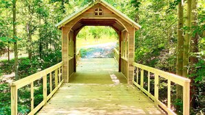 A wooden covered bridge with a simple, rustic design, surrounded by lush greenery. - The Lake House: Dock|Marine Hammock|Screen Porch (Prospect Hill)