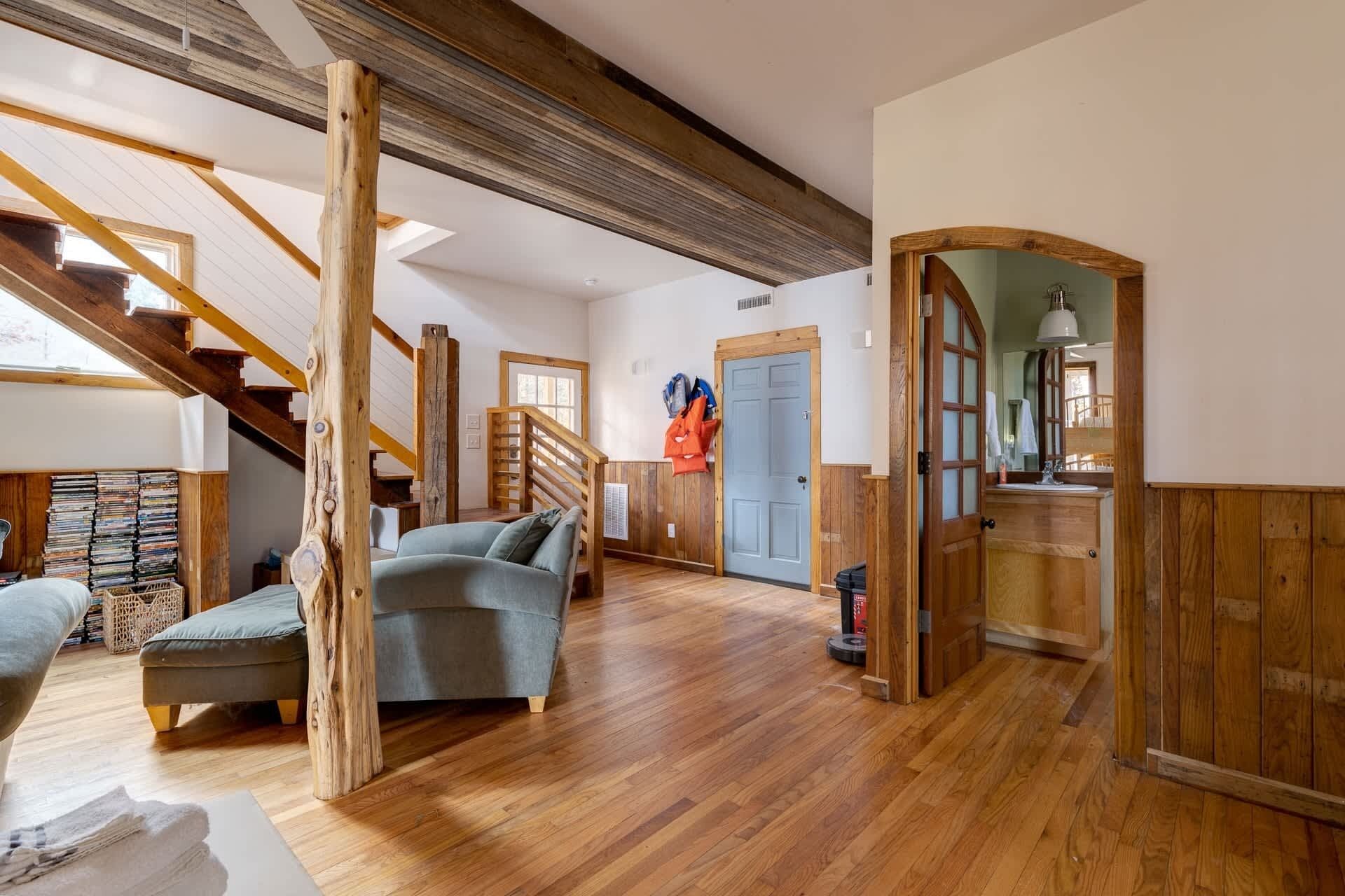 Amplia sala de estar con escalera de madera, un sofá y una puerta que da a un baño.