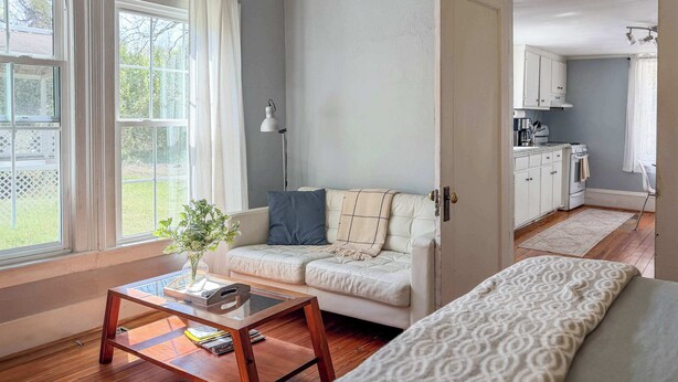 A modern living room with a sofa, a coffee table, and a view of a kitchen. - Studio with Deck, Walk to Duke (Durham)