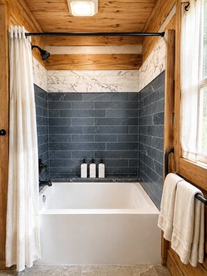 Une salle de bain avec une baignoire, des murs recouverts de carreaux foncés, un plafond en bois et une fenêtre avec un rideau.
