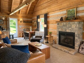 A log cabin interior with a fireplace, wooden dining area, and a cozy seating arrangement. - Scenic Log Cabin in Meadows of Dan (Meadows of Dan)