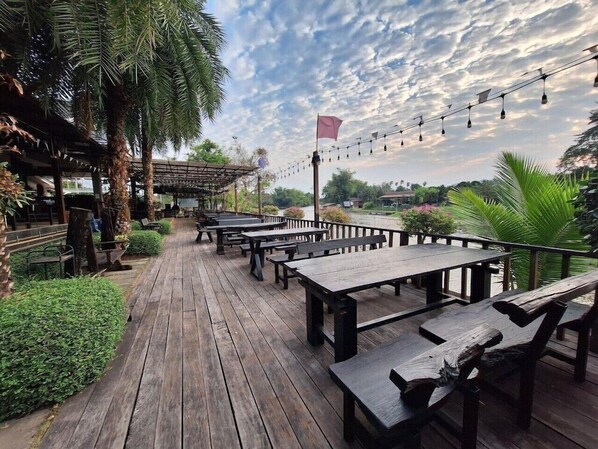 Un patio exterior con mesas y bancos de madera, rodeado de vegetación y vistas al cielo.
