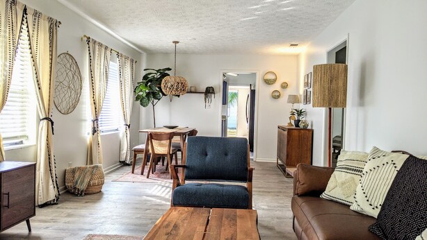 A living room with a wooden coffee table, a blue armchair, a brown sofa, and a dining area with a table and chairs.