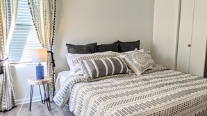 A neatly made bed with patterned bedding, a bedside table with a lamp, and curtains with geometric designs.