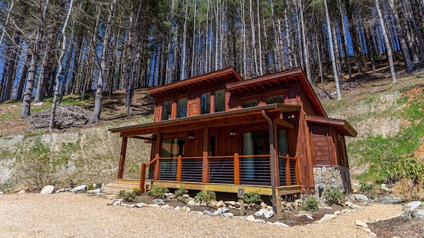 A wooden cabin with a balcony, surrounded by a forest.