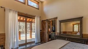 A bedroom with a large bed, a dresser, a mirror, and a sliding glass door leading to a balcony.
