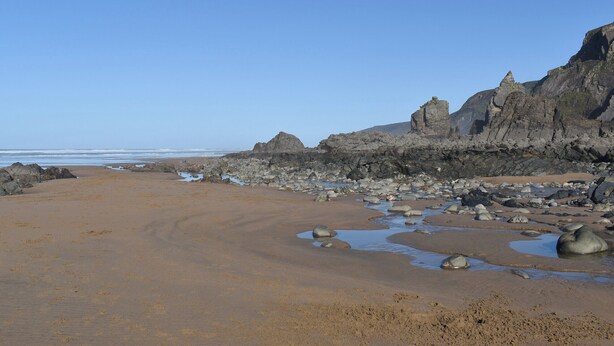 Een strand met rotsen en heldere lucht.