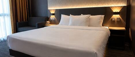 A modern hotel room with a large bed, two bedside tables, a wall-mounted light, and a view of the outdoors.