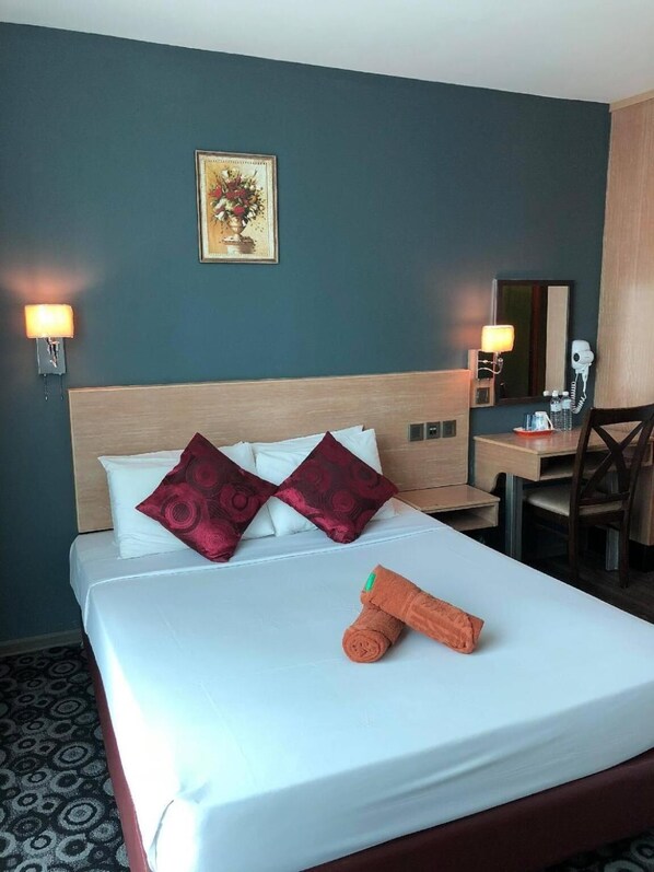 A hotel room with a bed, two wall-mounted lamps, a desk with a chair, a mirror, and a framed picture on the wall.