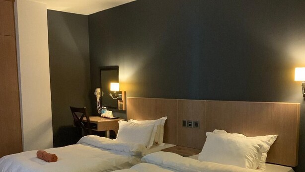 Een hotelkamer met twee bedden, een houten hoofdeinde, een nachtkastje en een spiegel.