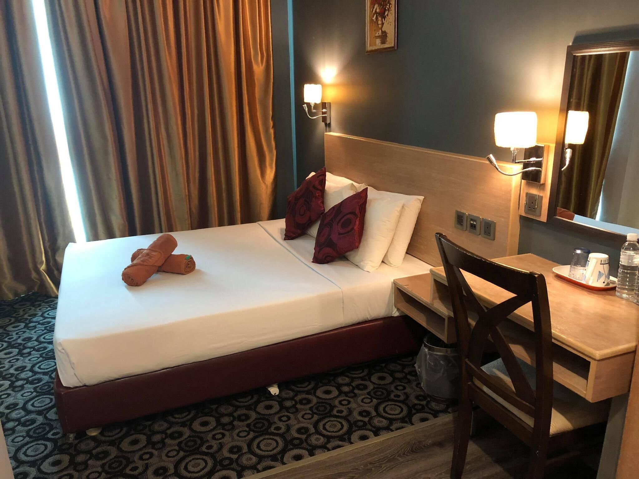 Une chambre d’hôtel équipée d’un lit, d’un bureau, d’une chaise, d’une poubelle et d’un miroir.