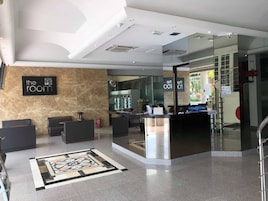 Un vestíbulo de hotel con mostrador de recepción, zona de estar y un letrero que dice 'the room'.