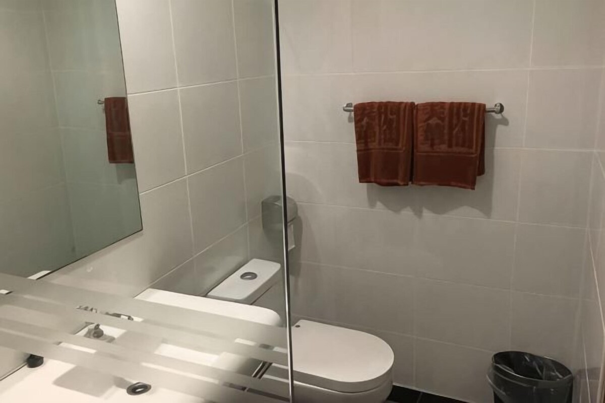 A bathroom with a glass partition, a white toilet, and two towels on a rack.