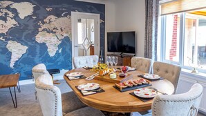 A dining area with a round wooden table set for six, surrounded by upholstered chairs. A world map mural adorns the wall behind the table.