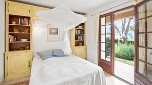 Ein Schlafzimmer mit Bett, Baldachin, Bücherregalen und Blick ins Freie.