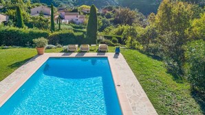 Ein rechteckiger Pool mit Steinbord, umgeben von einer Rasenfläche mit einigen Liegestühlen und einer Pflanze im Topf.