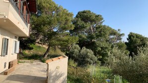A building with a balcony, a pathway leading to the entrance, and surrounding greenery including trees and shrubs. - Villa Alfonso with sea view (Siculiana)